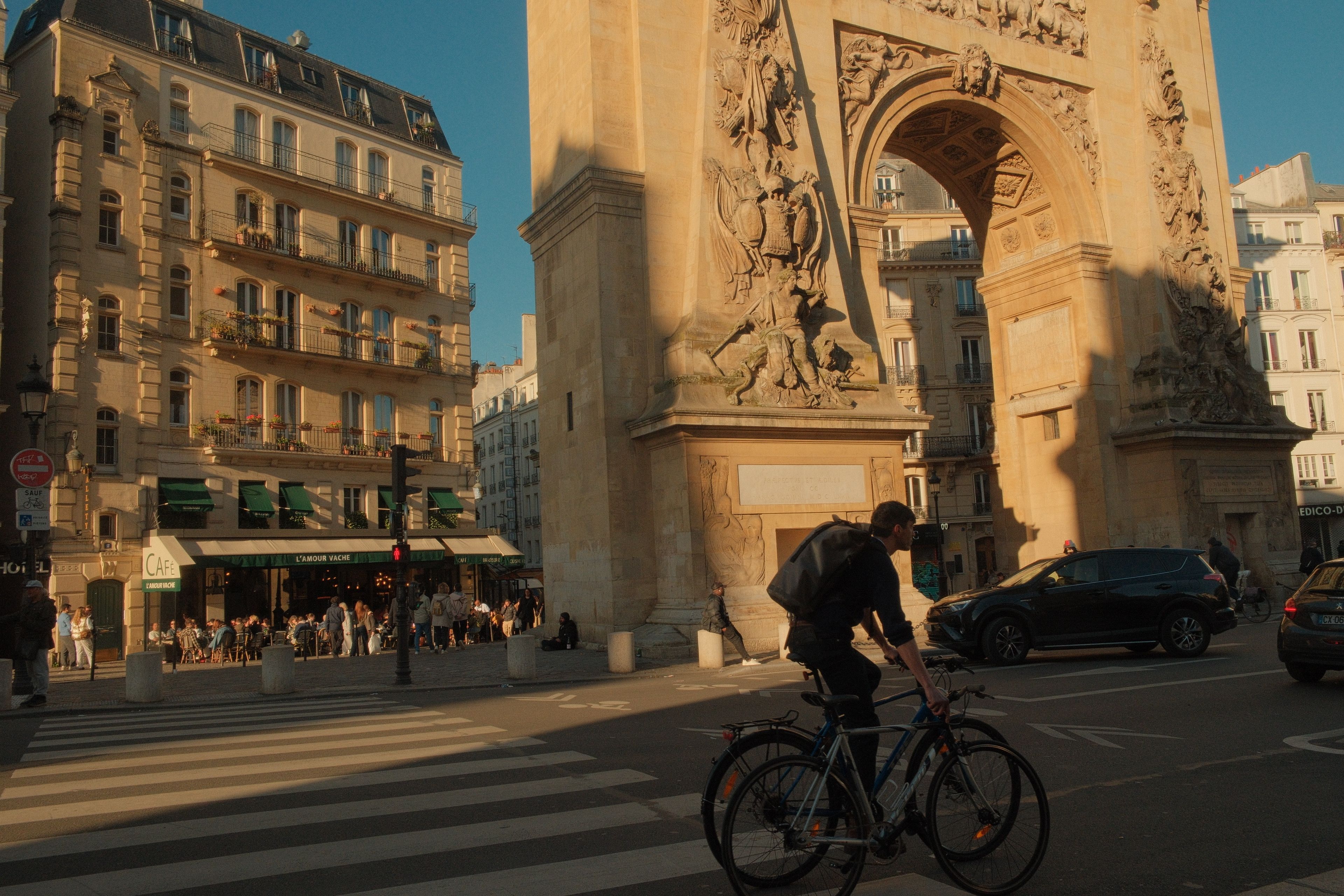 A vibrant street scene at Porte Saint-Denis in Paris with a cyclist at sunset.