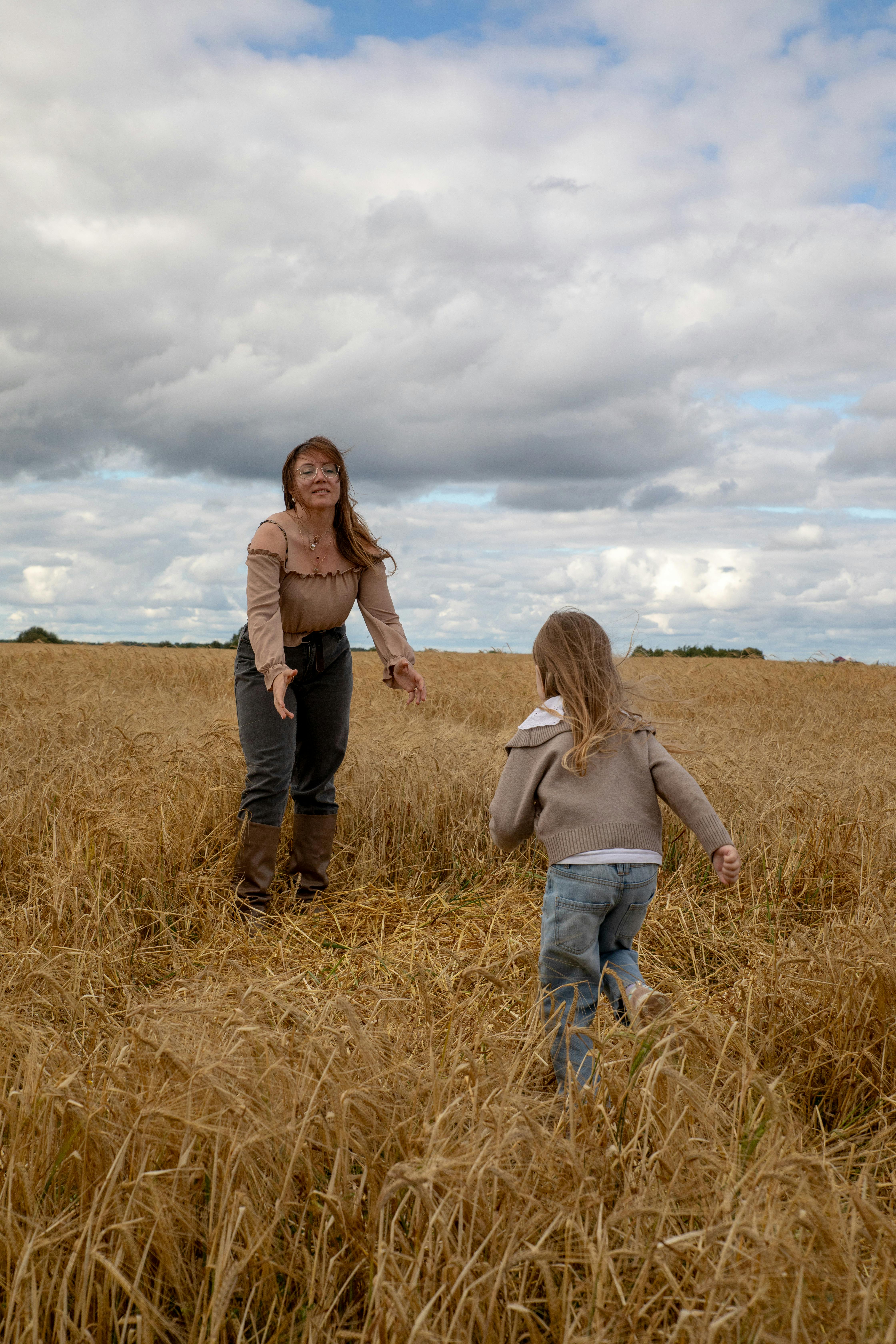 Joyful moment of a mother and daughter in a golden wheat field under a cloudy sky.