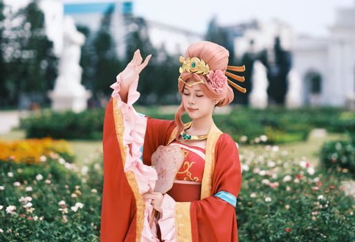 A woman in traditional costume poses gracefully in a lush garden setting.