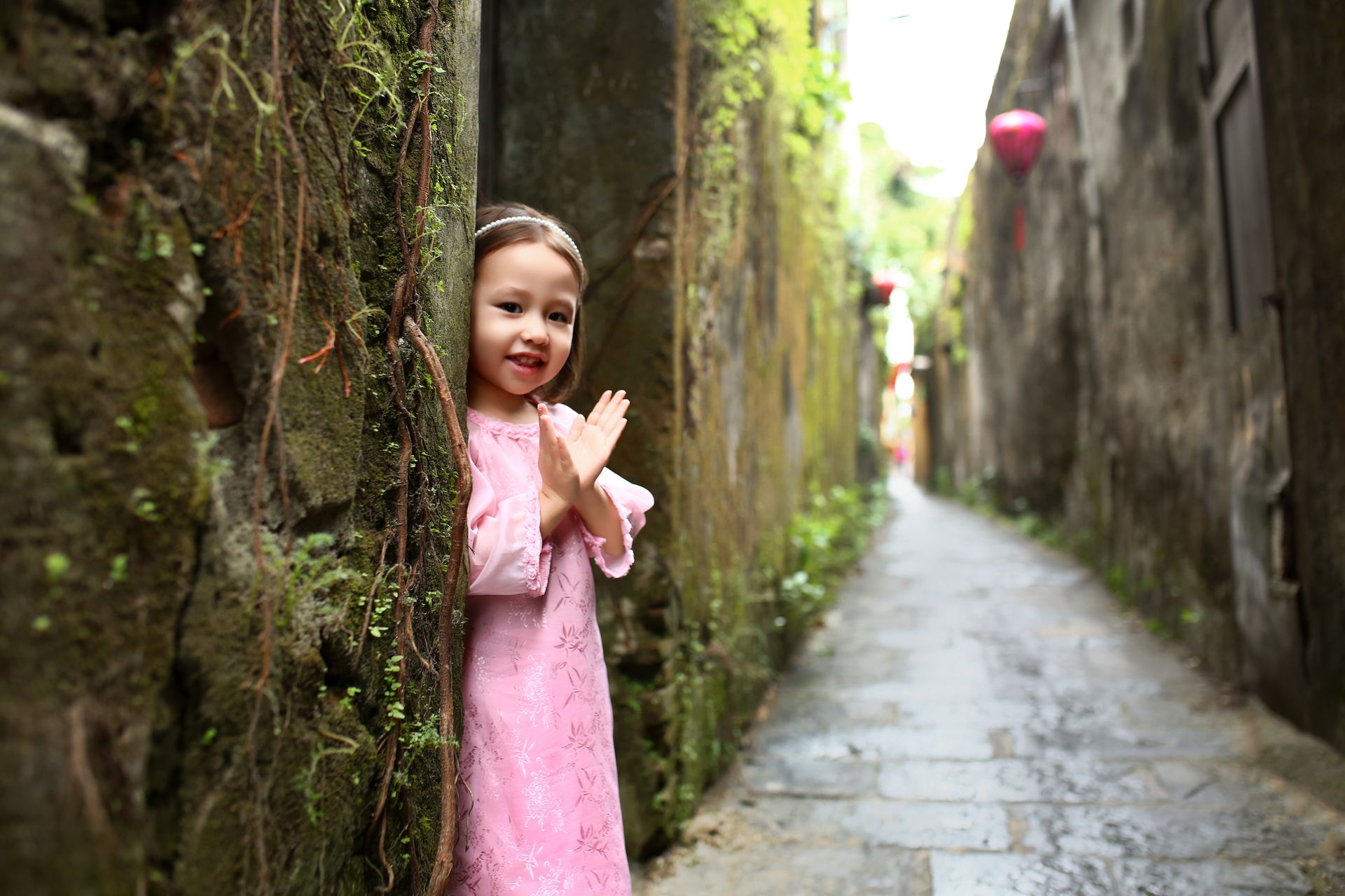 Adorable child in traditional attire smiles in a Hội An alley, captured with a Canon EOS 5D Mark III.