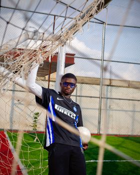 A young male footballer in sports attire posing confidently next to a goal on a sunny day.