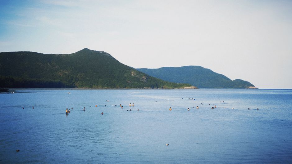 People enjoy swimming in a tranquil beach setting with lush green hills in the distance.