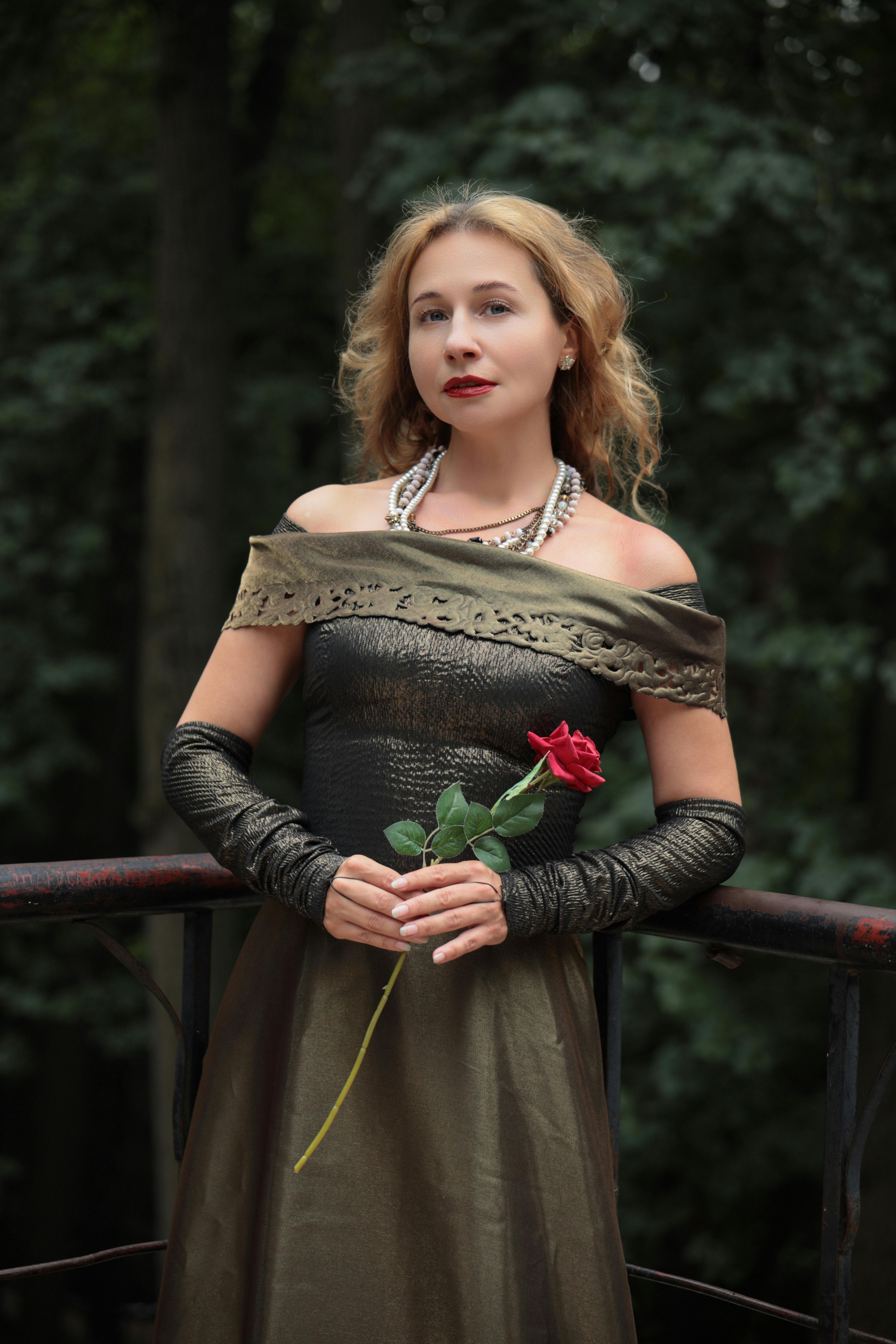 Elegant woman in vintage green dress holding a red rose on a balcony
