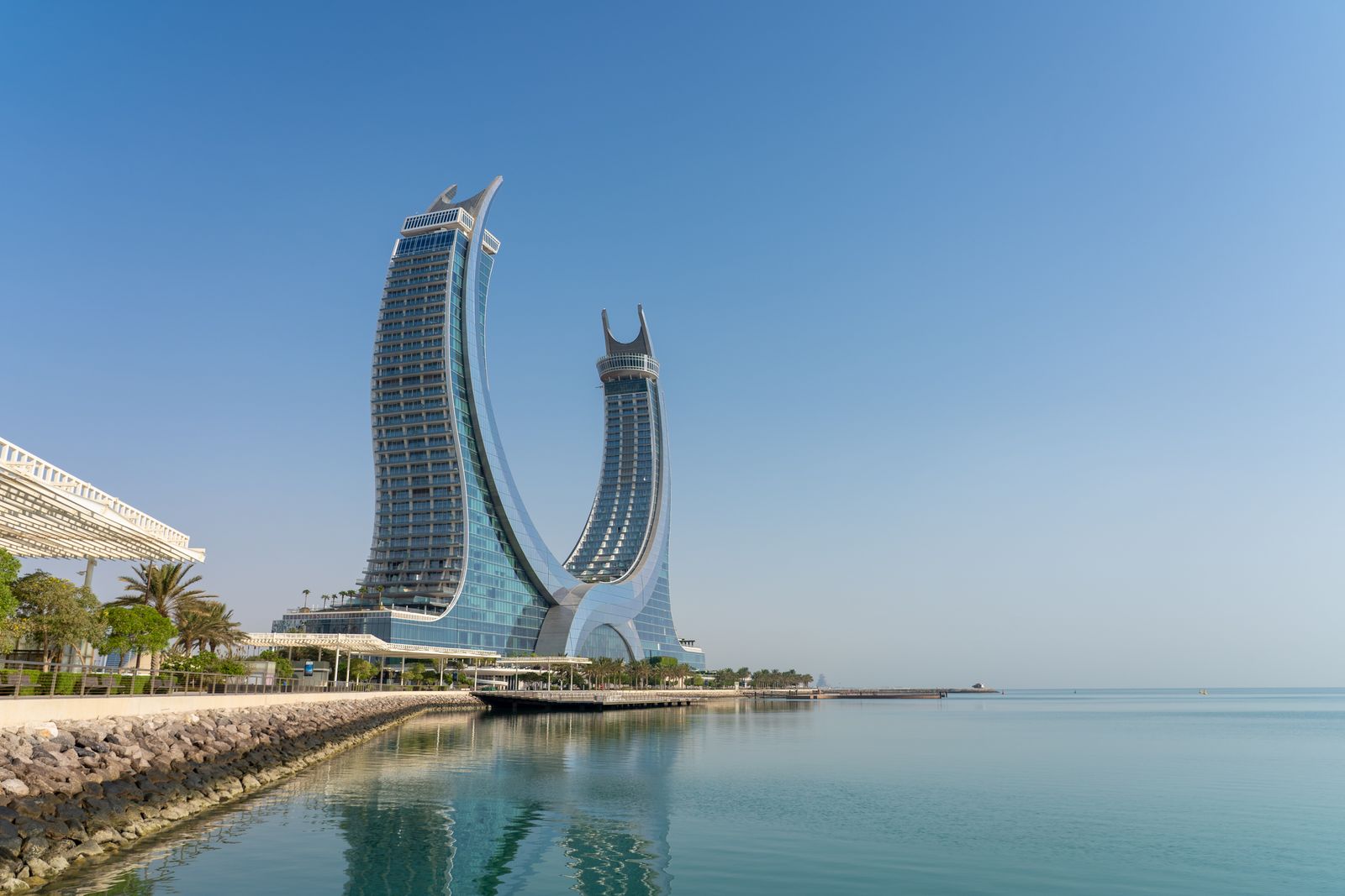 The striking Katara Towers in Lusail, Doha reflected in serene waters under a clear blue sky.
