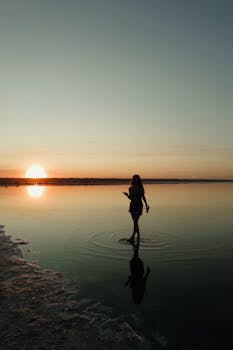A lone figure creates ripples in the tranquil waters of an Odessa lake at sunset, enveloped in natural beauty.