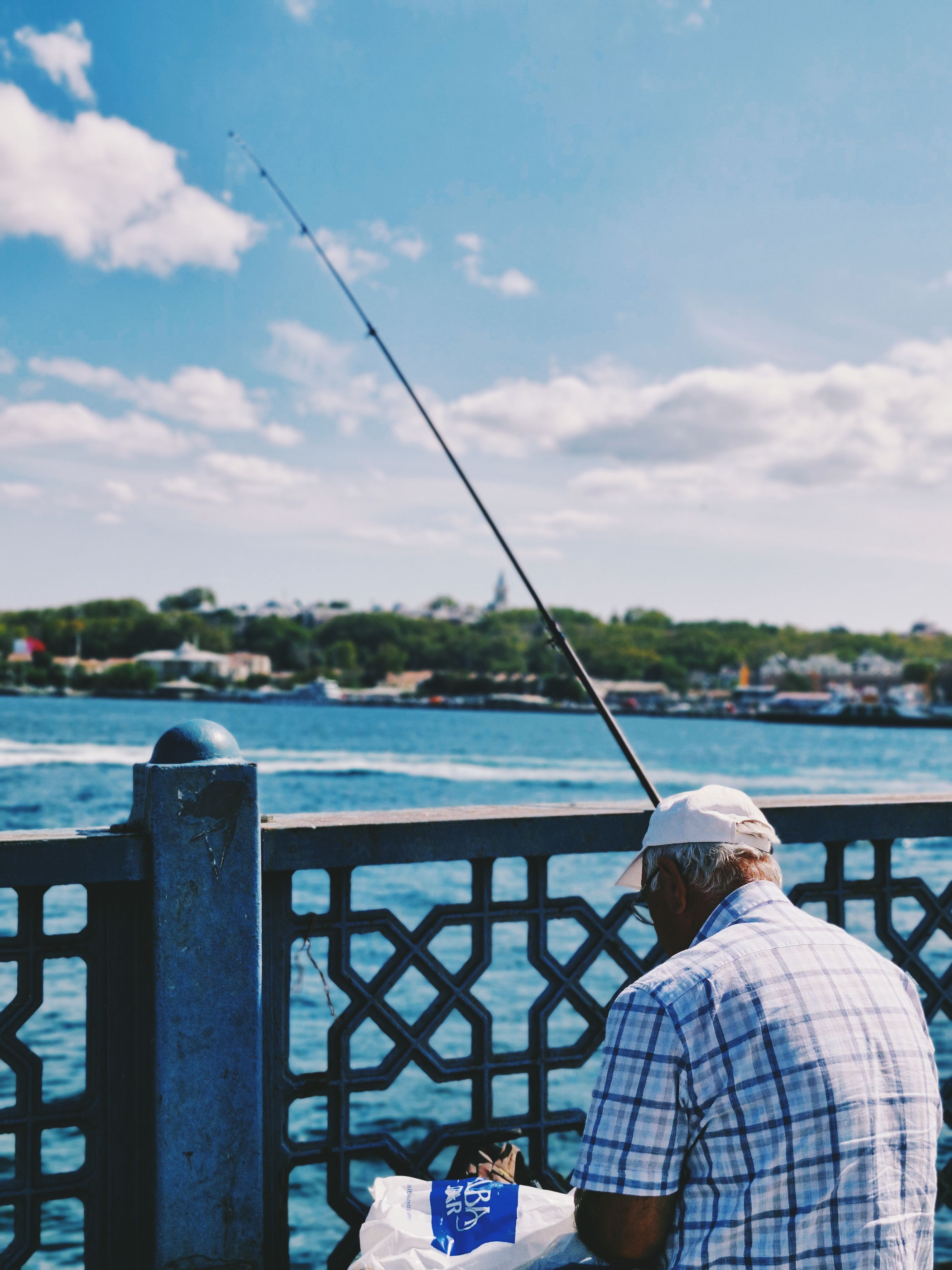 An elderly man fishing on Galata Bridge in Istanbul on a sunny day, capturing a classic scene.