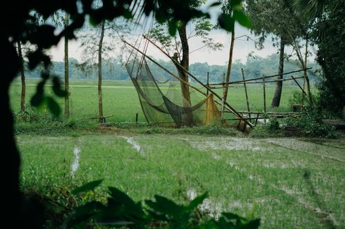 Free Serene rural scene with a traditional fishing net set against lush green fields and trees, perfect for nature themes. Stock Photo