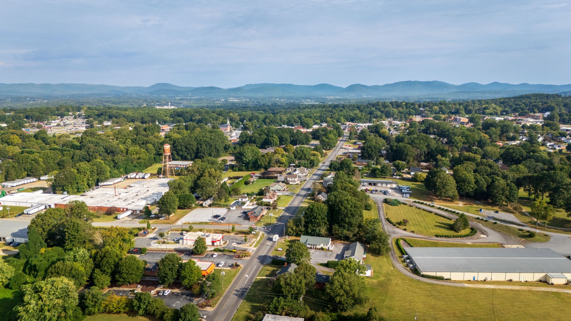 Aerial scenery of a town with lush greenery and distant mountains under clear skies.