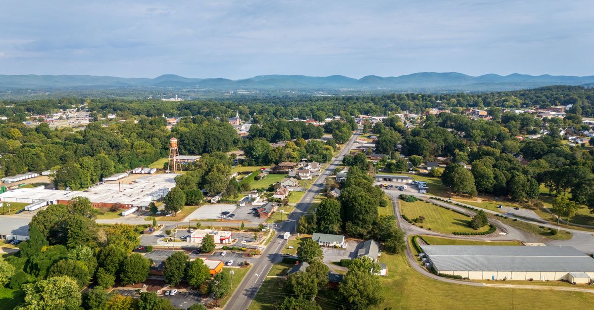Aerial scenery of a town with lush greenery and distant mountains under clear skies.