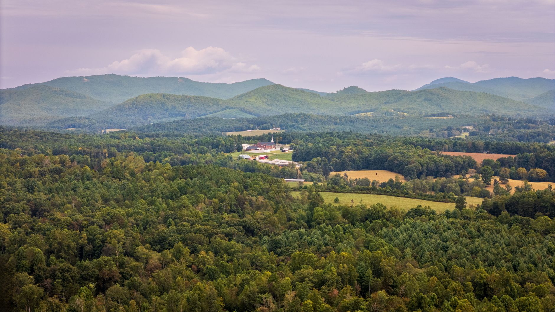 Aerial view of lush greenery and distant Appalachian Mountains under a cloudy sky.