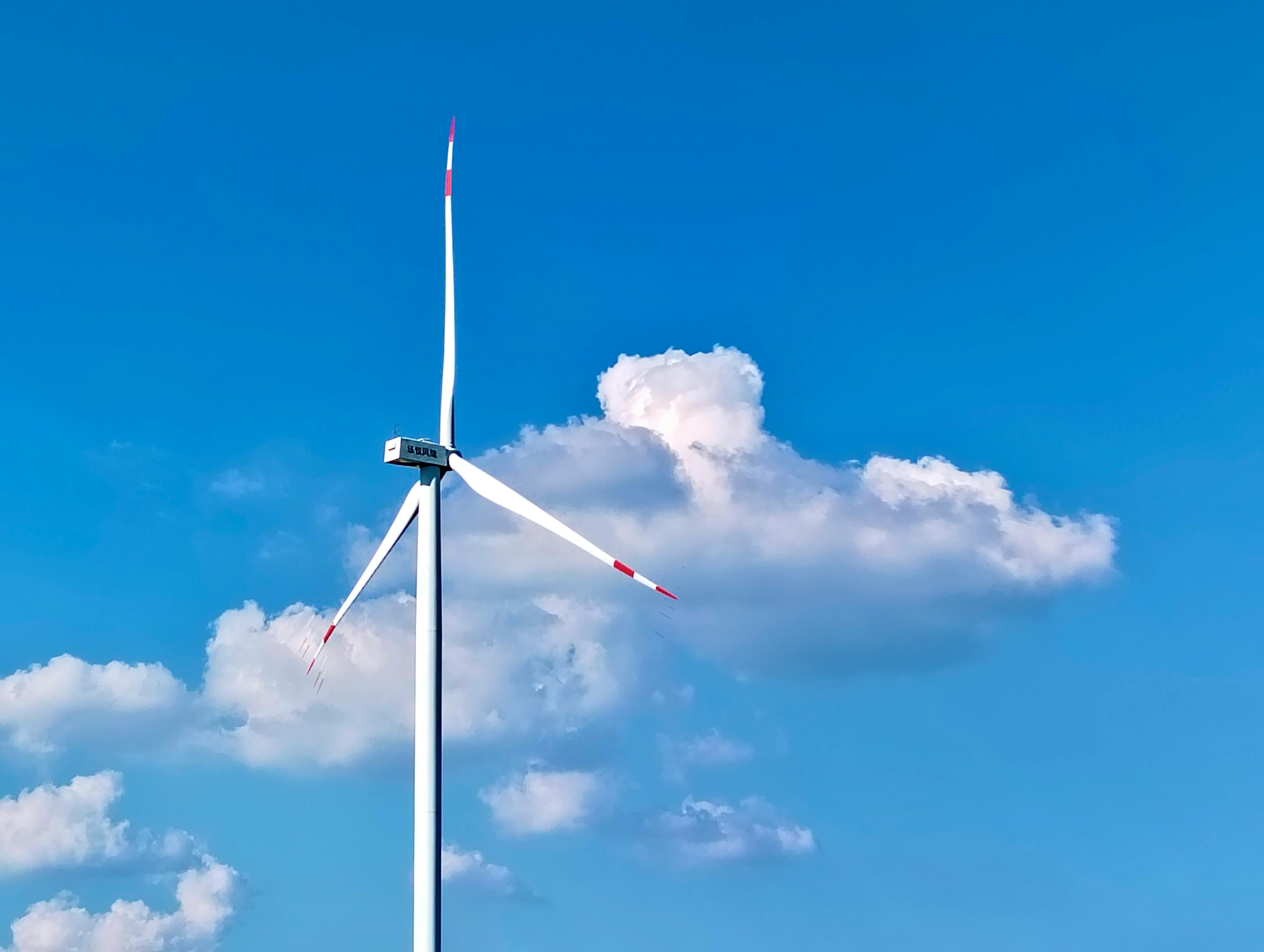 A wind turbine stands tall against a bright blue sky with fluffy clouds, showcasing renewable energy.