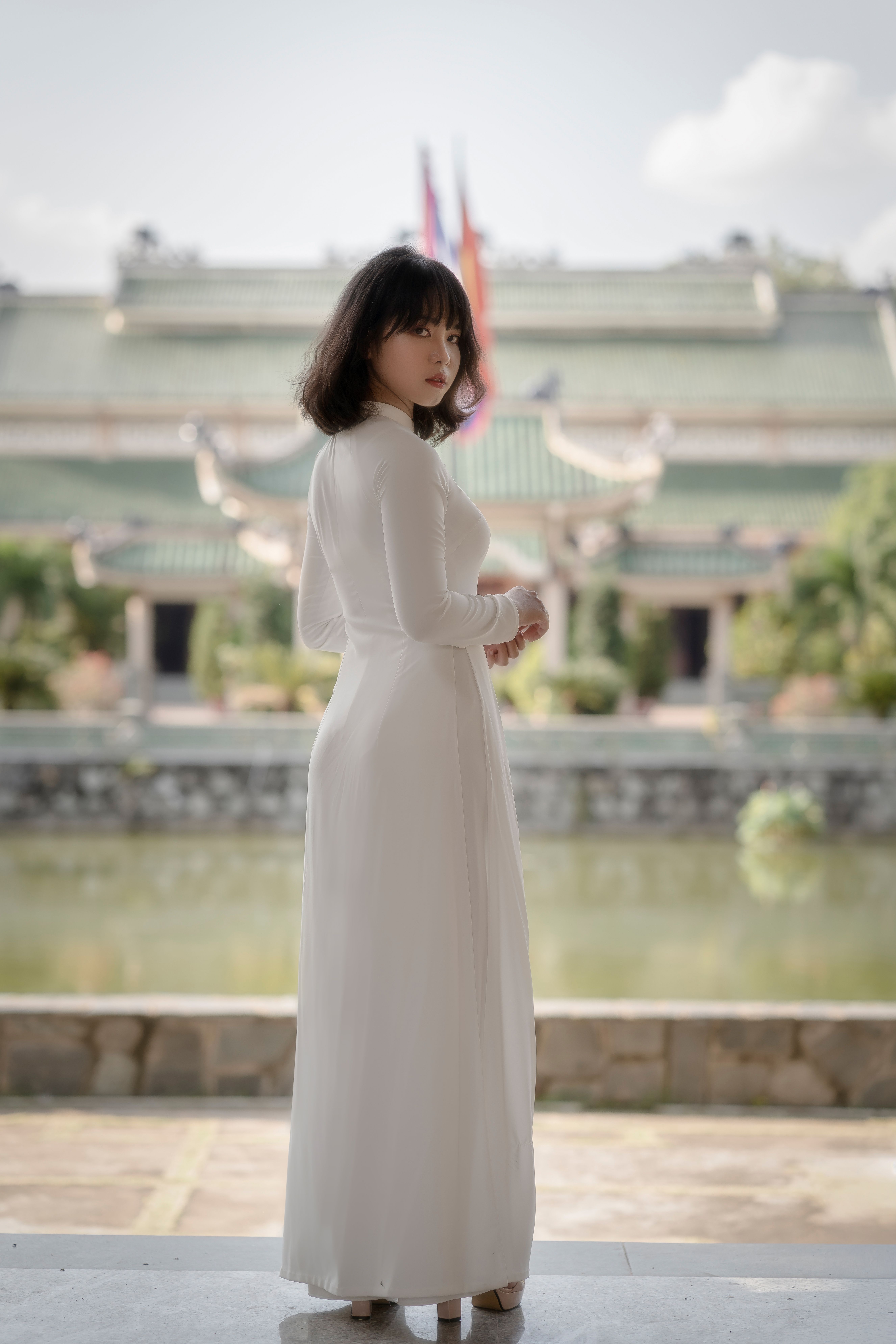 A woman in a white traditional dress poses gracefully outdoors in front of a cultural building.