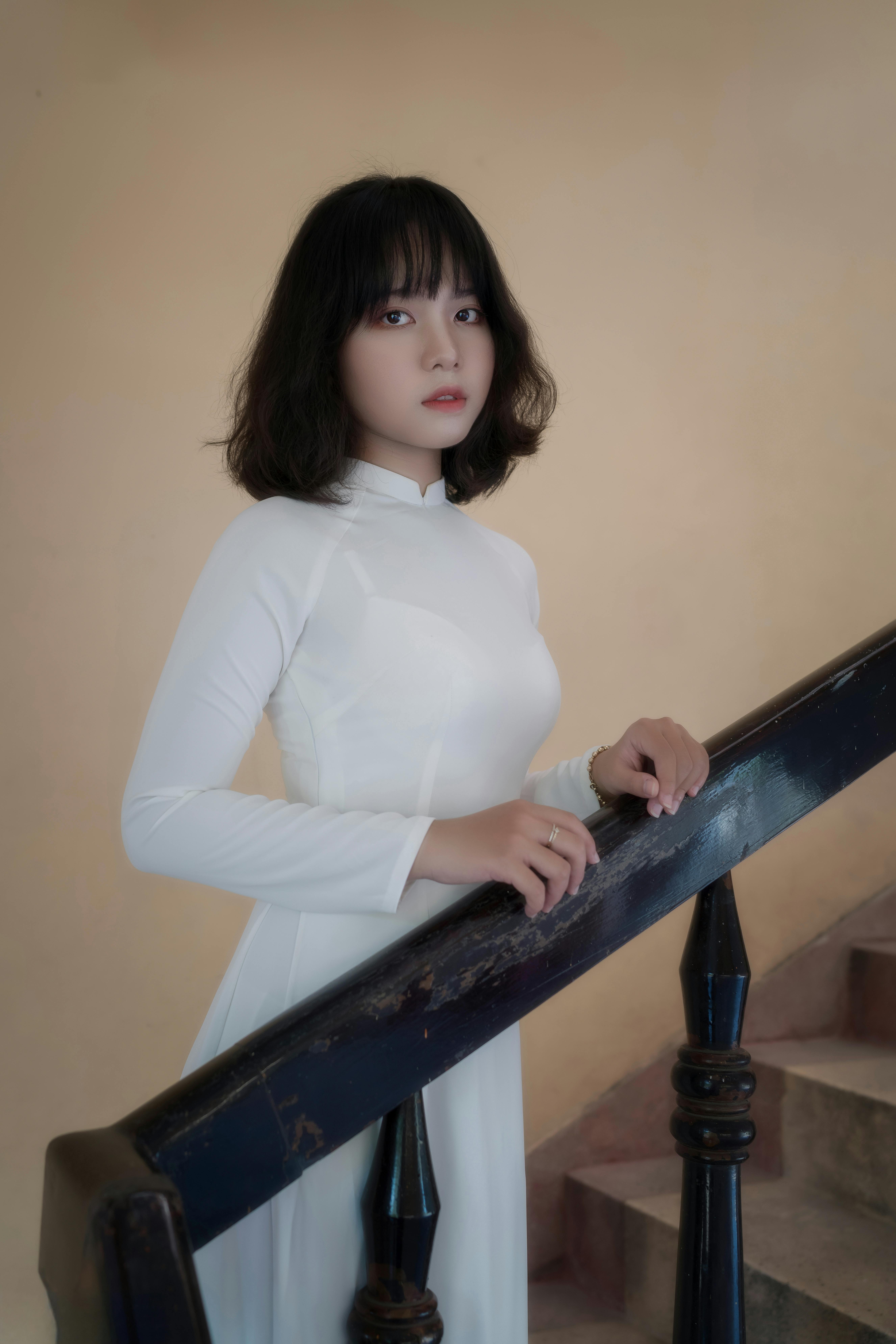 Portrait of a woman in a white ao dai standing on stairs with a soft expression.