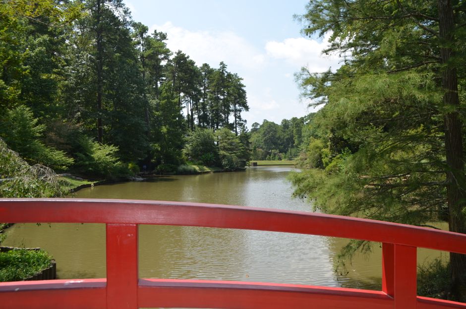A picturesque view from a red bridge over a calm river surrounded by lush greenery.