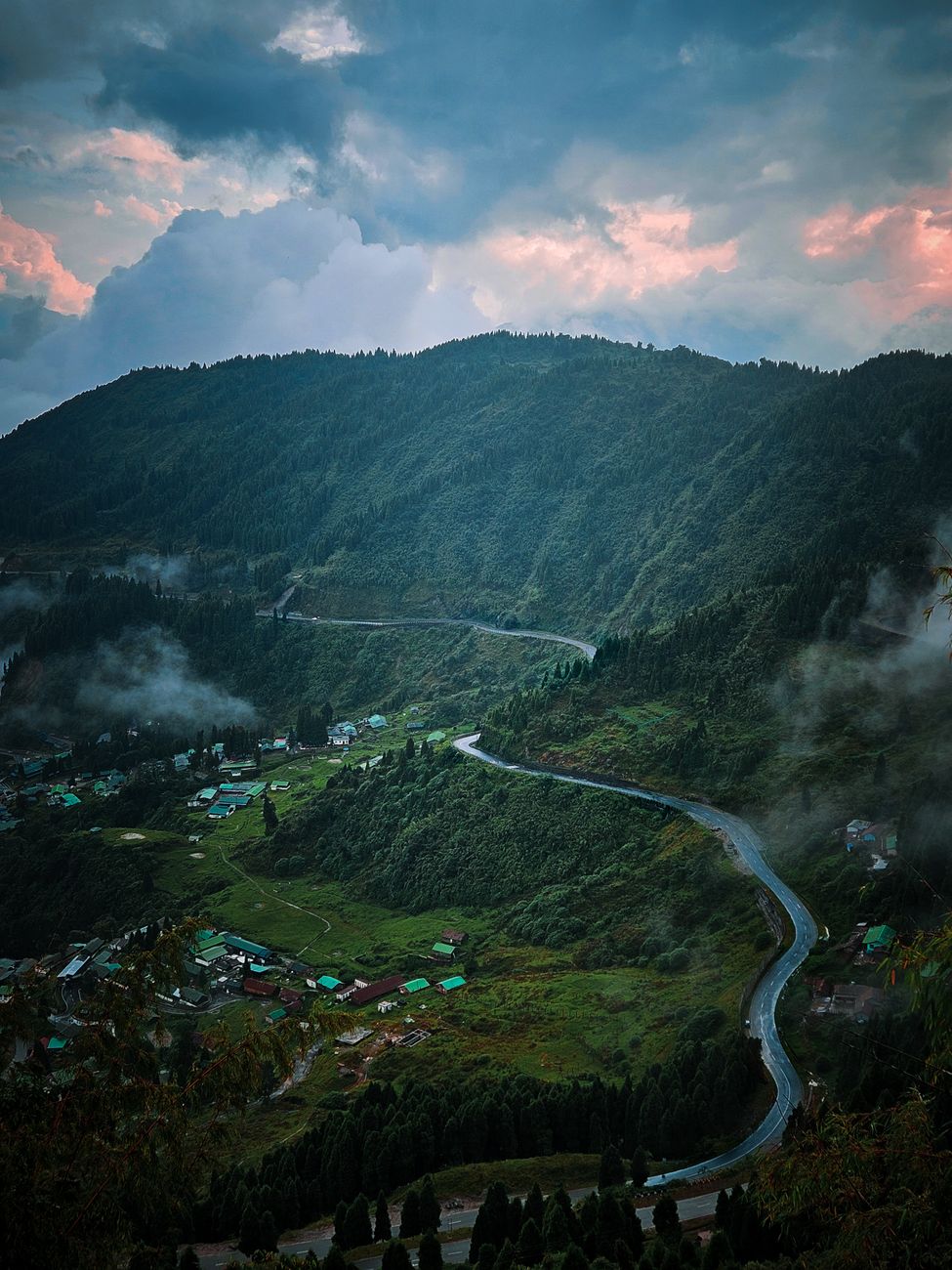 Serene view of winding road amidst lush green mountains and misty valleys at dusk.