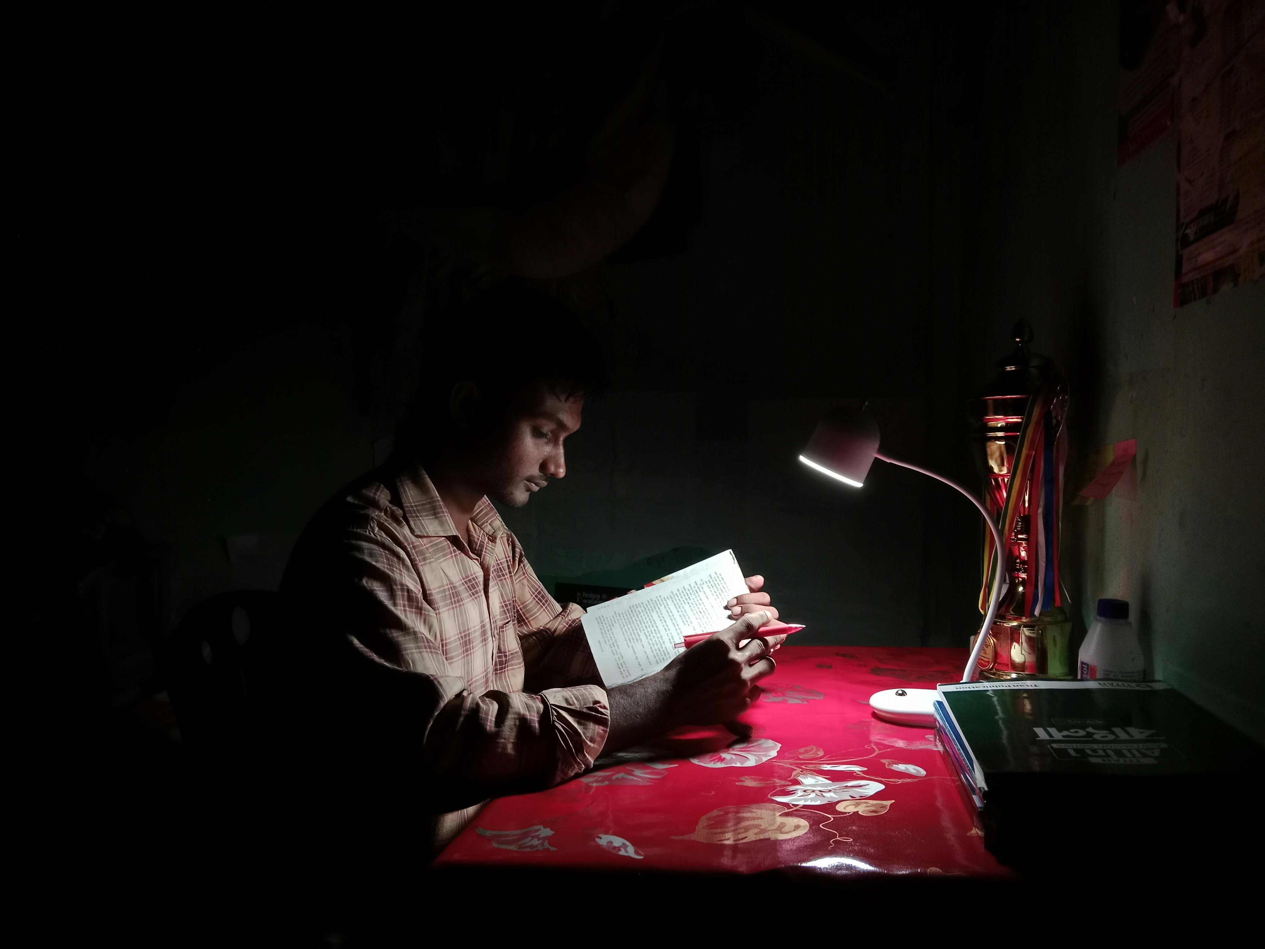 Student at a desk under a lamp in low ambient lighting
