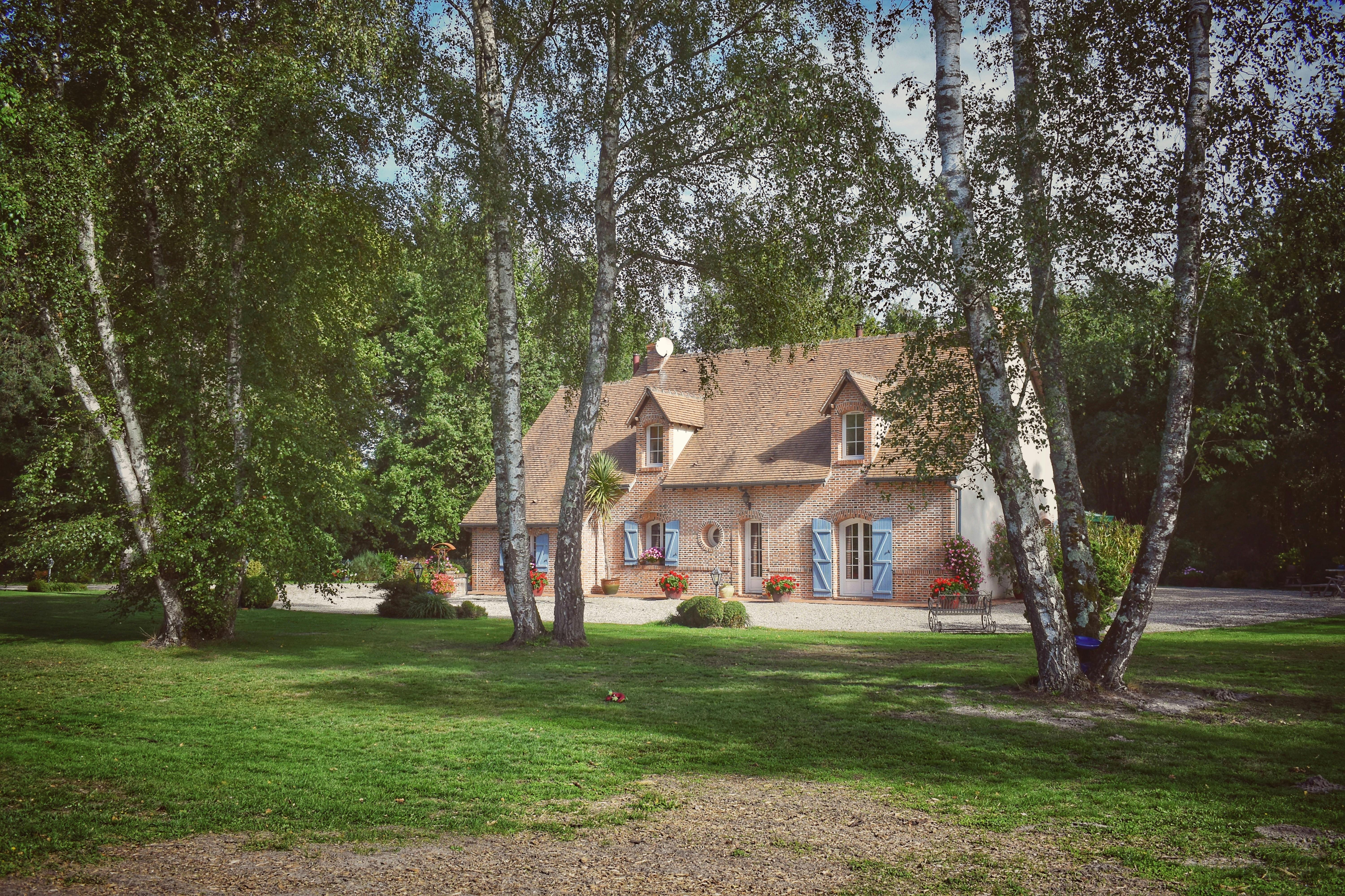 Beautiful cottage surrounded by trees and a manicured lawn, evoking a serene rural atmosphere.