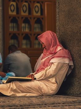 Man in traditional attire reading in Madinah mosque, showcasing cultural serenity.
