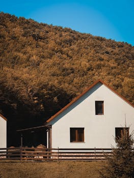 Tranquil white house nestled against a lush autumn forest, under a clear blue sky.