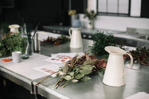 White Metal Pitchers on Table Top by Flowers