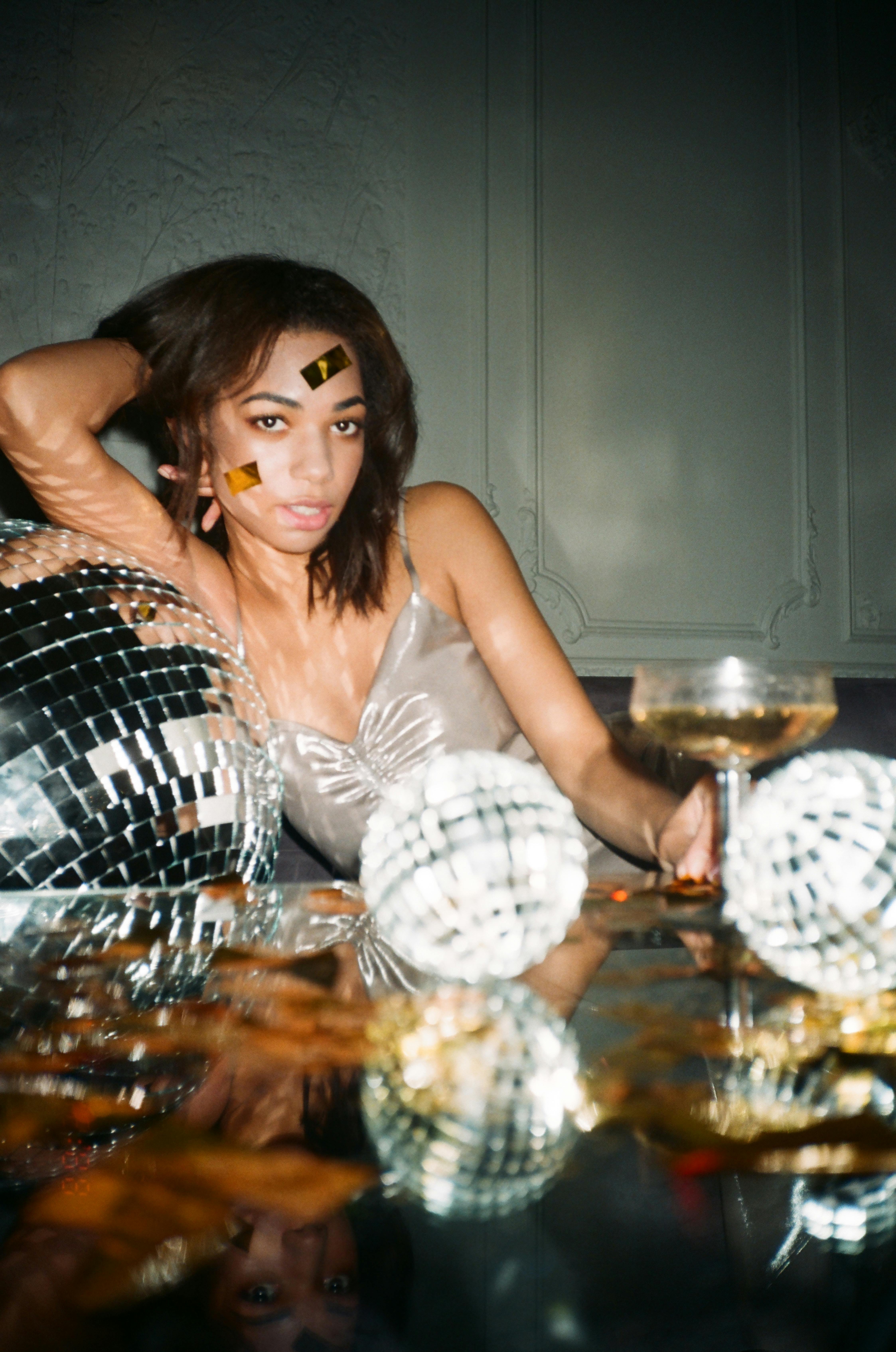 woman in gray top leaning to a mirror ball