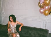 派对上，一位穿着金属连衣裙的时髦女人坐在沙发上，手拿气球喝着饮料