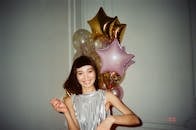 在室内派对上，一位微笑的女人手持彩色气球摆着姿势，散发着欢乐与庆祝的气息