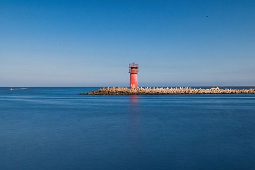 Free A vibrant red lighthouse stands on a tranquil coastline in Ras El-Bar, Egypt, under a clear blue sky. Stock Photo