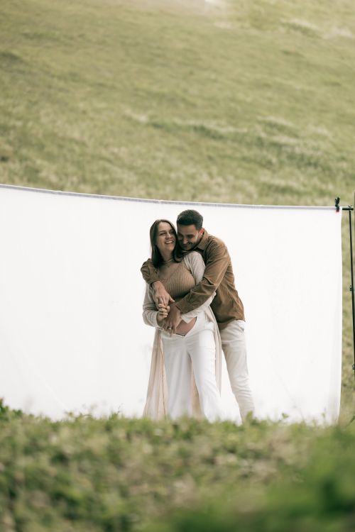 Free A loving couple embraces in front of a white backdrop outdoors, expressing romance and joy. Stock Photo
