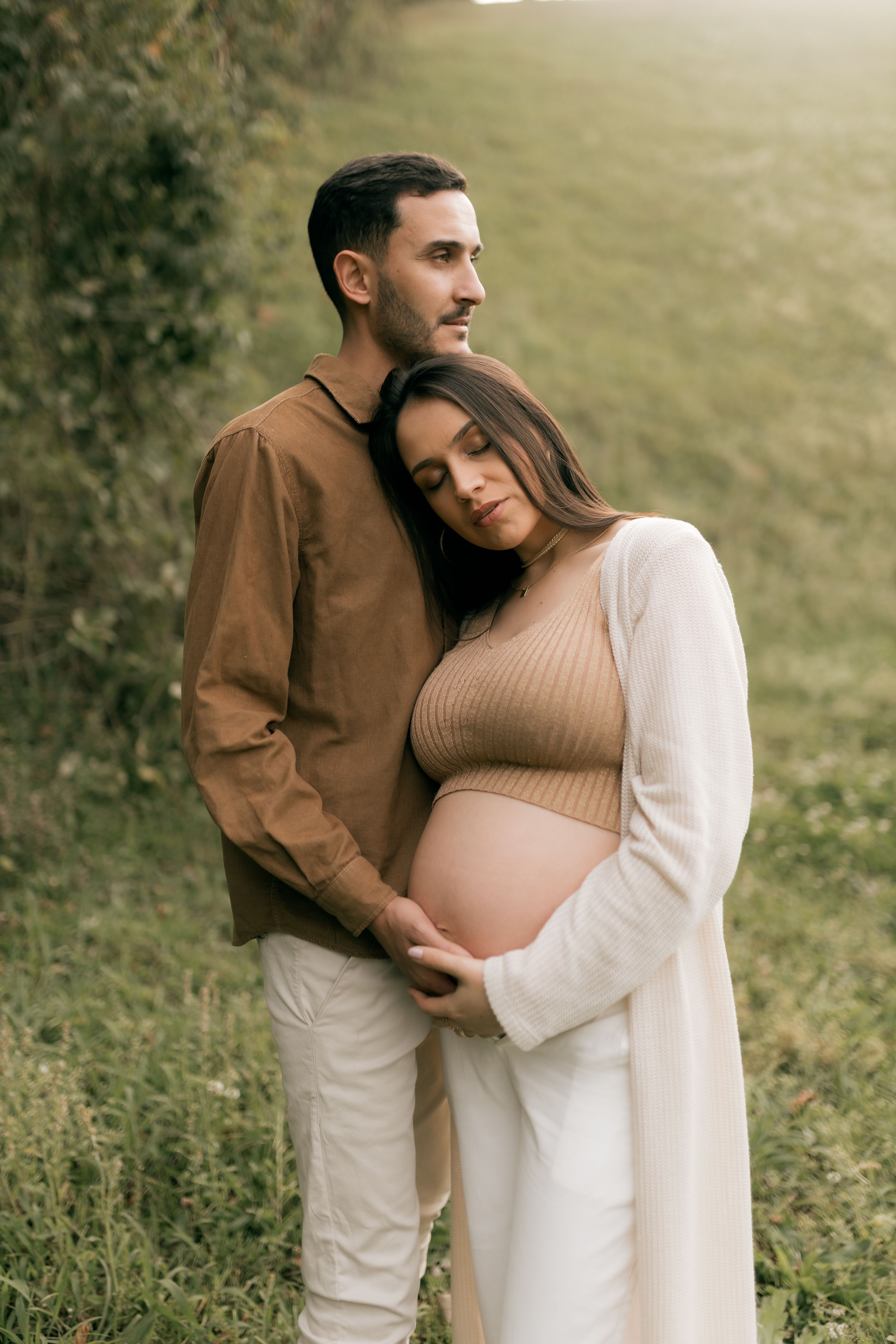 A loving couple embraces outdoors, highlighting an expectant mother's pregnancy in a serene setting.