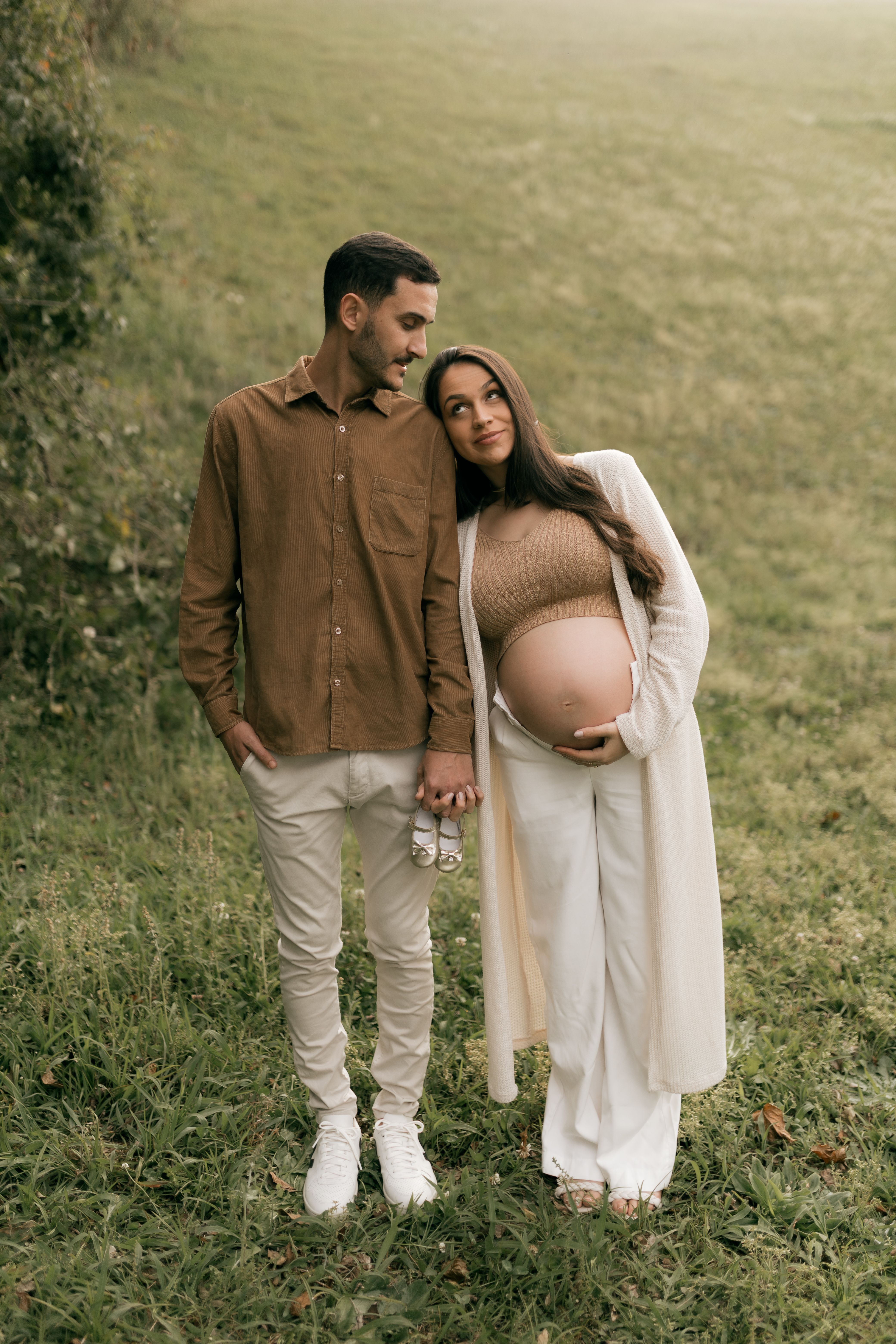 A loving couple expecting a baby, sharing an affectionate moment outdoors, dressed in stylish neutral tones.