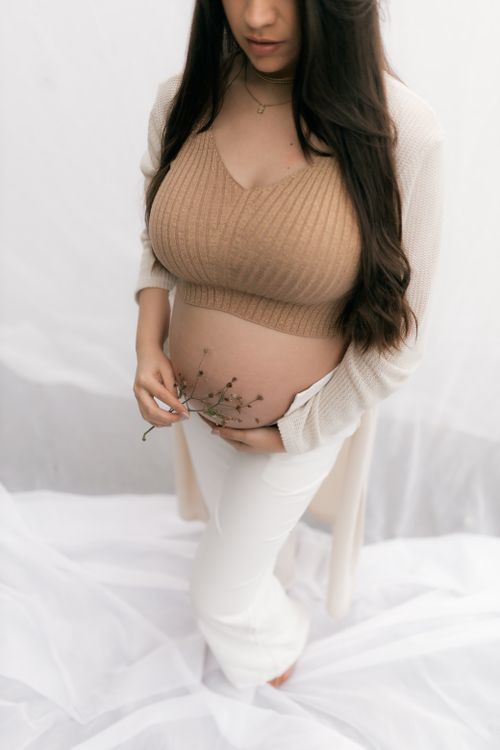 Free A serene maternity portrait featuring a woman holding delicate flowers over her belly, embracing new life. Stock Photo