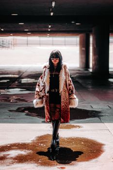 Fashionable woman in a fur coat walking through an urban setting, showcasing bold style and winter fashion.