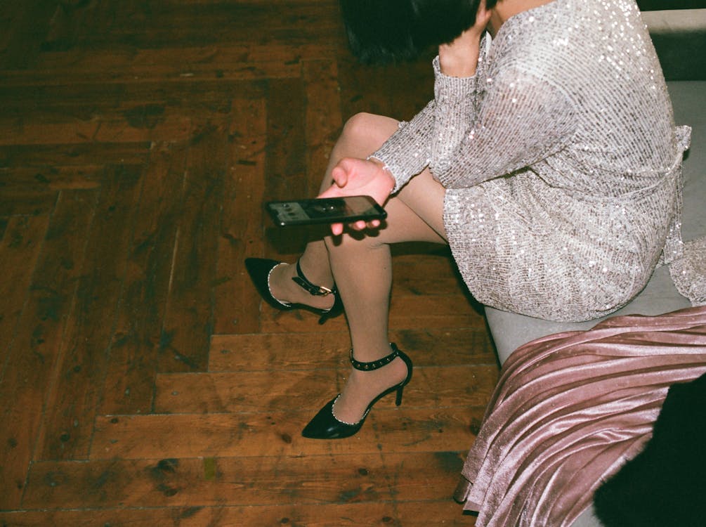 woman in a fancy dress at party sitting on a couch looking at her phone.
