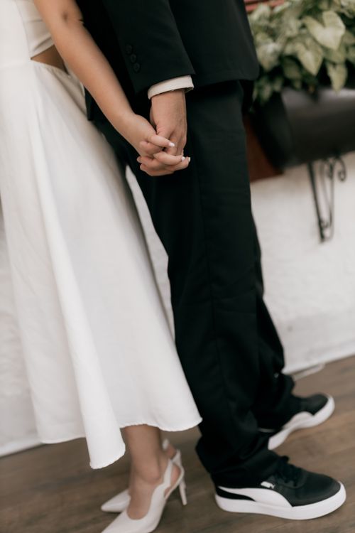 Free Bride and groom holding hands showcasing unique wedding style with sneakers and formal wear. Stock Photo