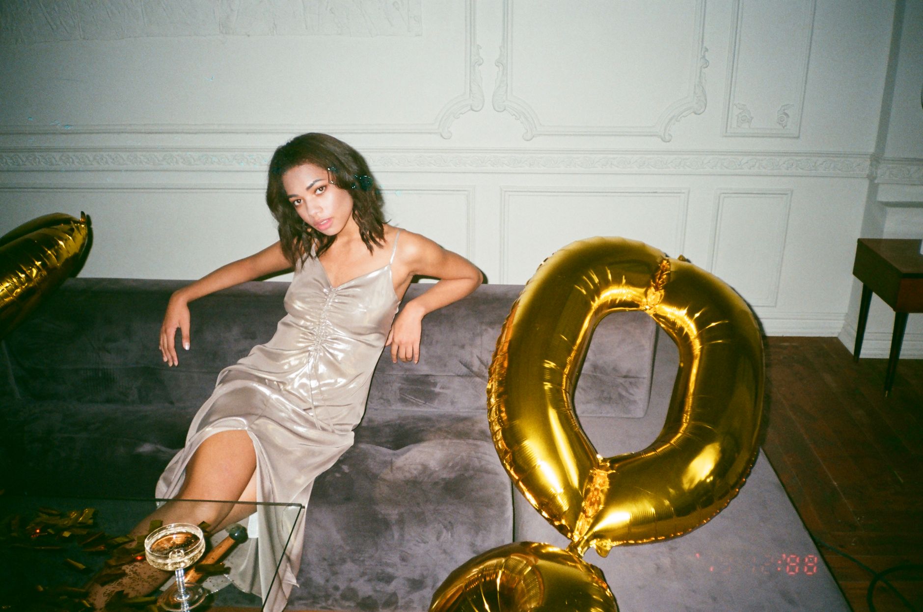 Woman in satin dress sitting with a gold balloon, exuding elegance and party vibes.
