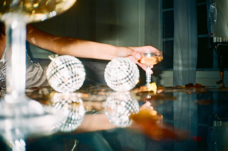 A festive indoor scene with champagne glass and shiny ornaments reflecting light on a table.