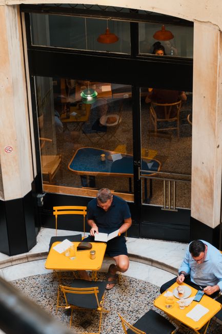 An inviting outdoor cafe setting with two men dining and reading, creating a relaxed atmosphere.