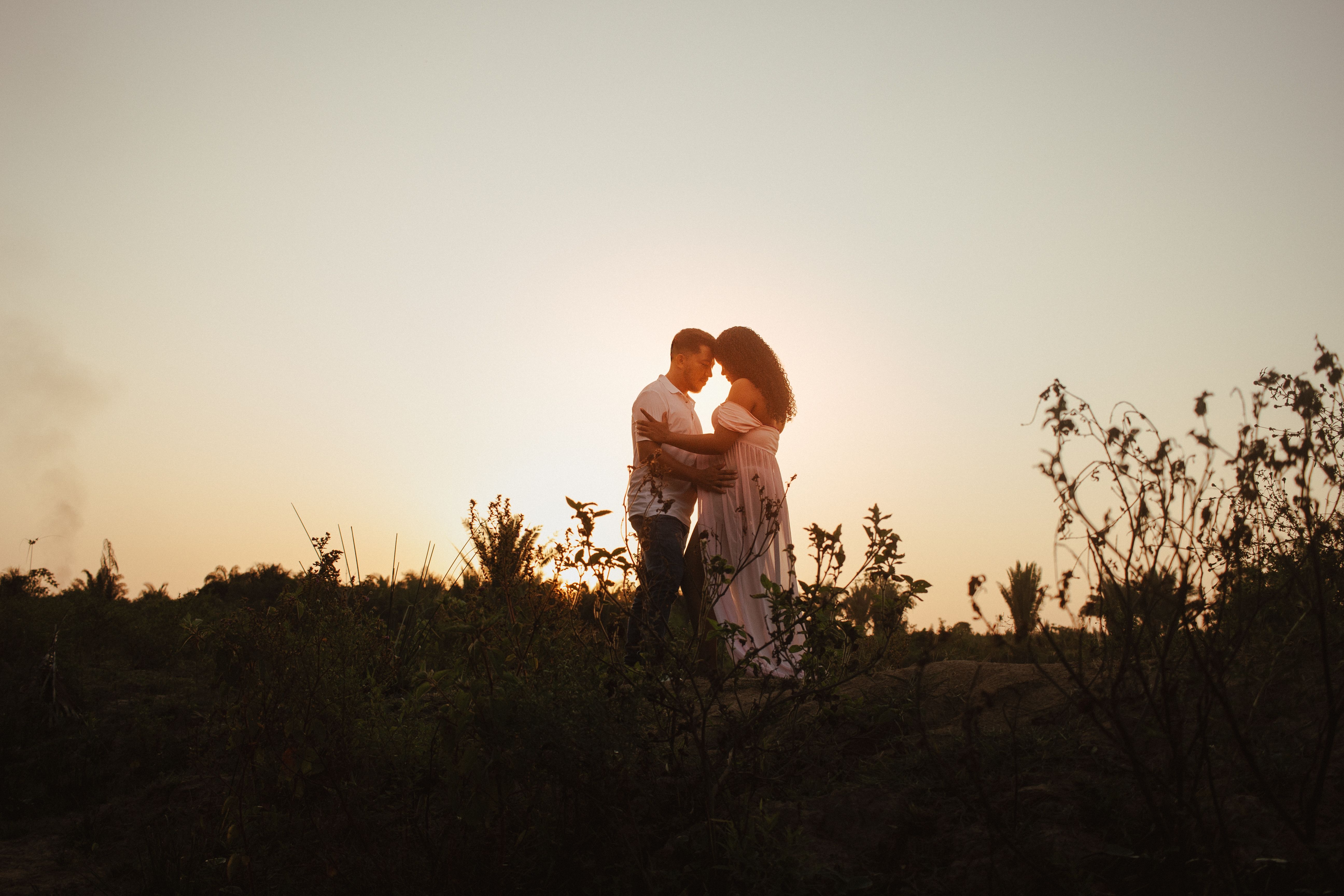 Couple embracing outdoors during a warm sunset, celebrating pregnancy.