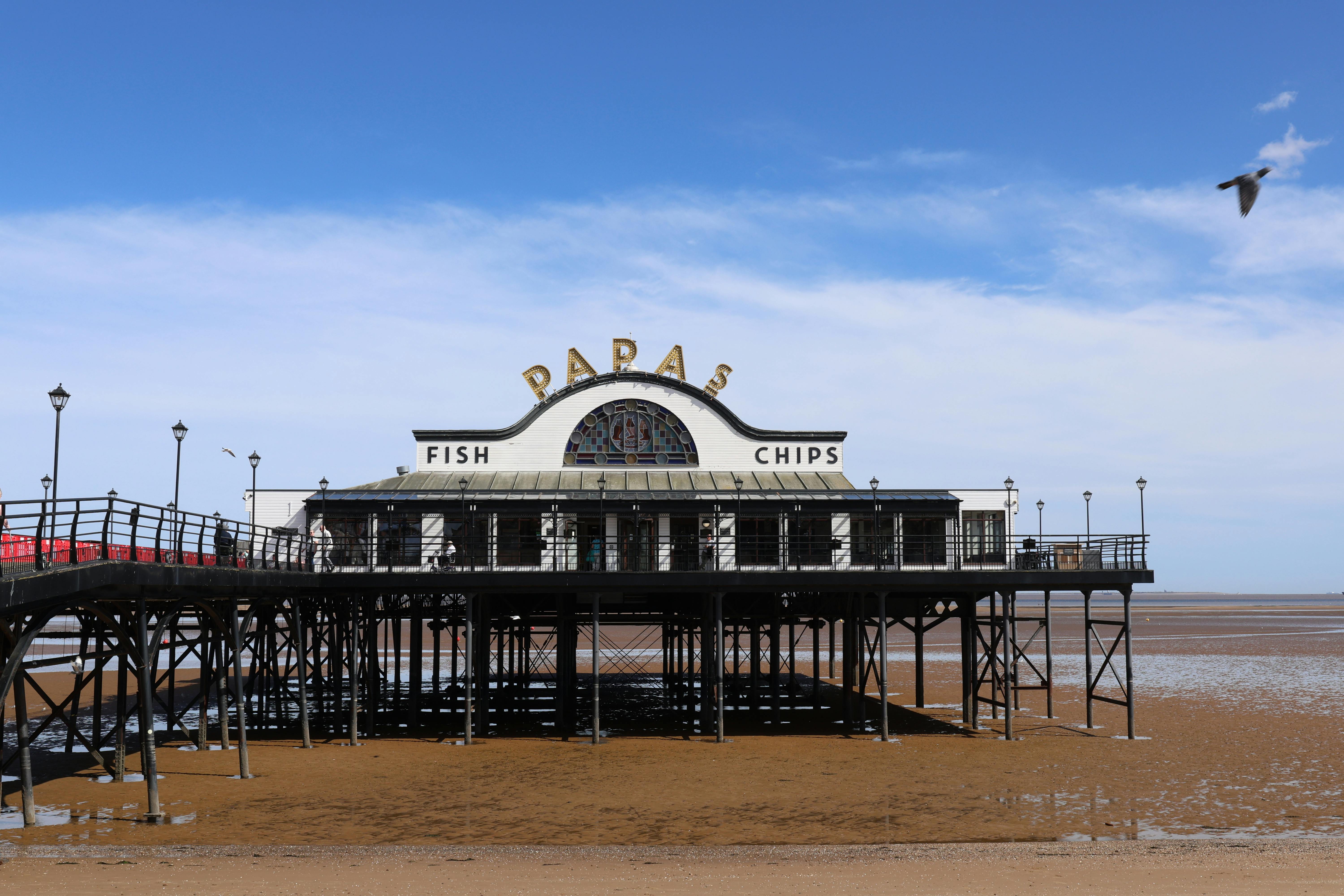 Classic view of Cleethorpes Pier with a fish and chips shop under a blue sky.
