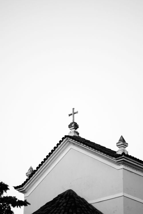 Free Minimalist black and white photo of a church roof with a cross against the sky. Stock Photo