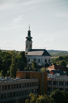 A picturesque view of a historic church surrounded by urban buildings and lush greenery in Hungary.