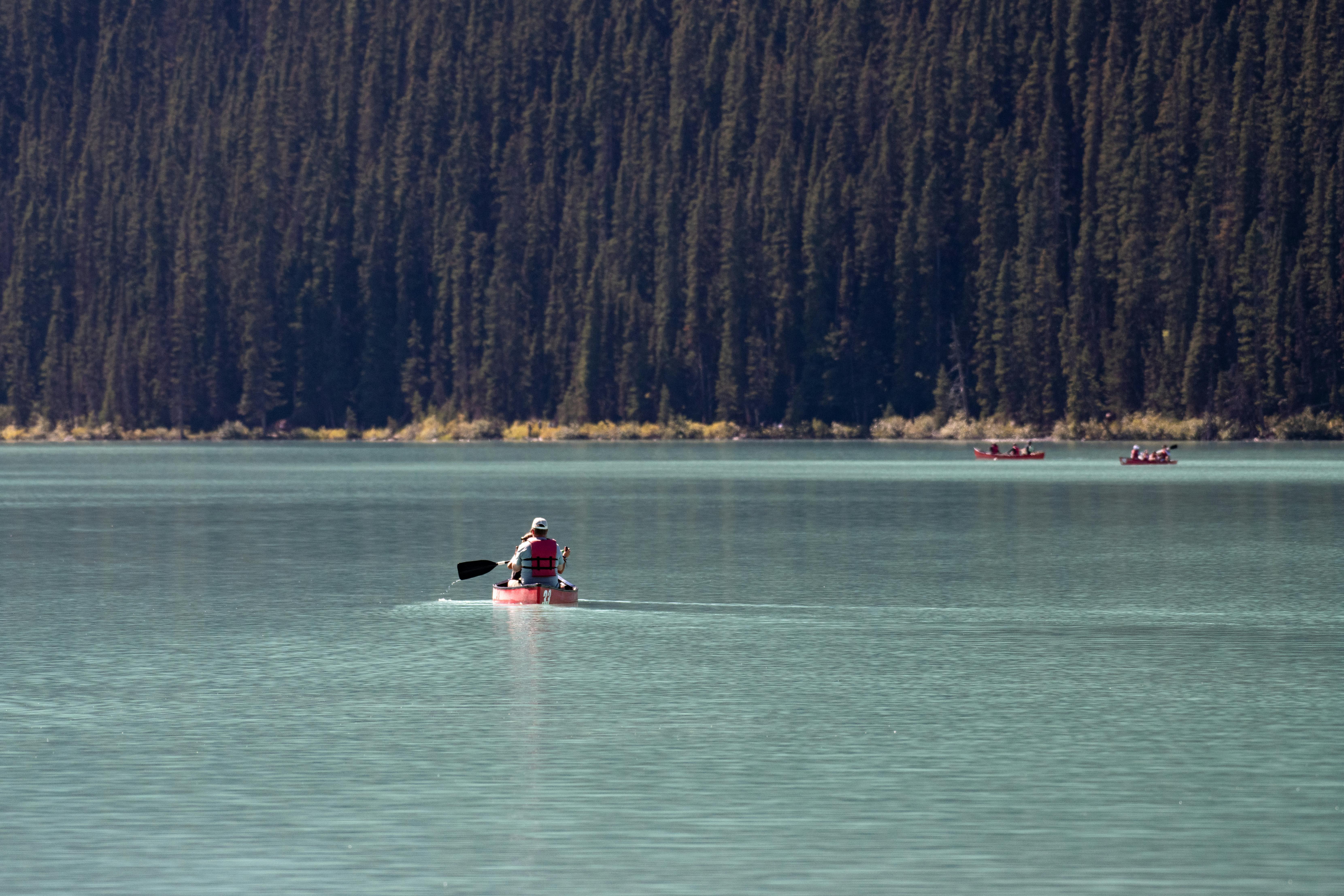 Canoers paddle across a serene mountain lake surrounded by dense forests.