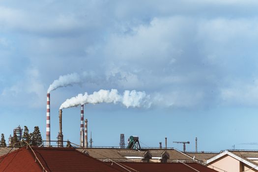 Factory chimneys emitting smoke over rooftops on a clear day, illustrating urban pollution.