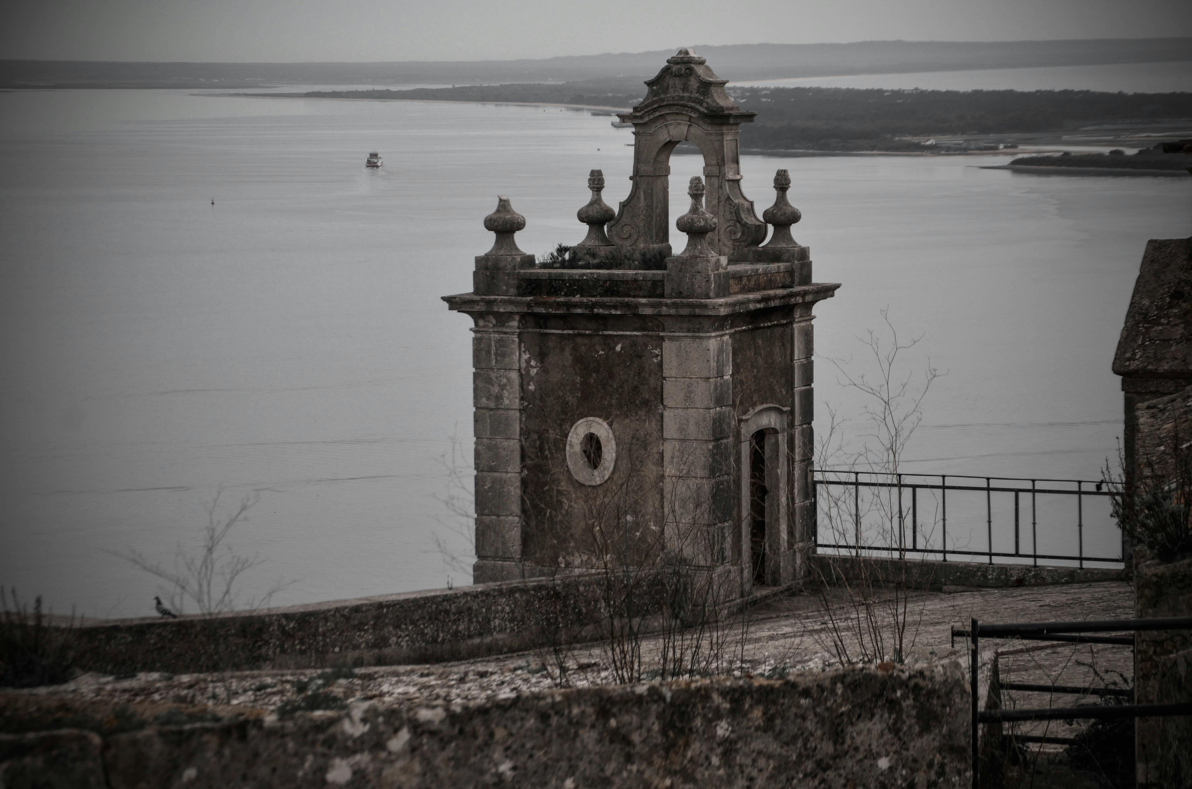 Vintage stone structure beside a calm lake under overcast skies, offering a peaceful view.