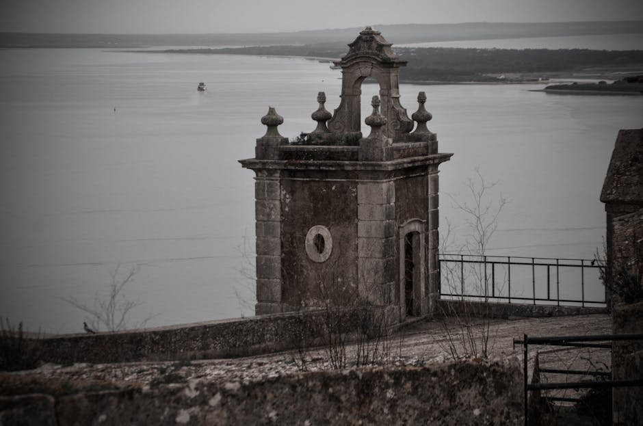 Vintage stone structure beside a calm lake under overcast skies, offering a peaceful view.