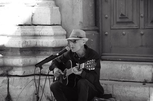 Free Black and white photo of a street musician playing guitar on stone steps with vintage ambiance. Stock Photo