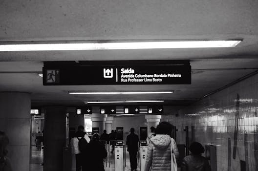 Monochrome photo of a subway station exit sign with people walking towards turnstiles.