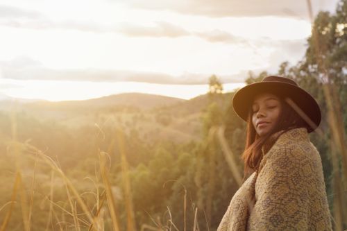 Free Woman wrapped in a blanket enjoying a tranquil autumn countryside view at sunset. Stock Photo