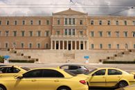 View of the Hellenic Parliament in Athens with yellow taxis in the foreground.
